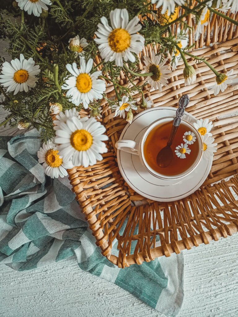 A cozy flatlay featuring chamomile tea in a cup, surrounded by fresh chamomile flowers on a wicker basket.